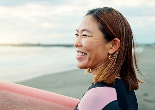 Woman smiling on a beach holding a surfboard